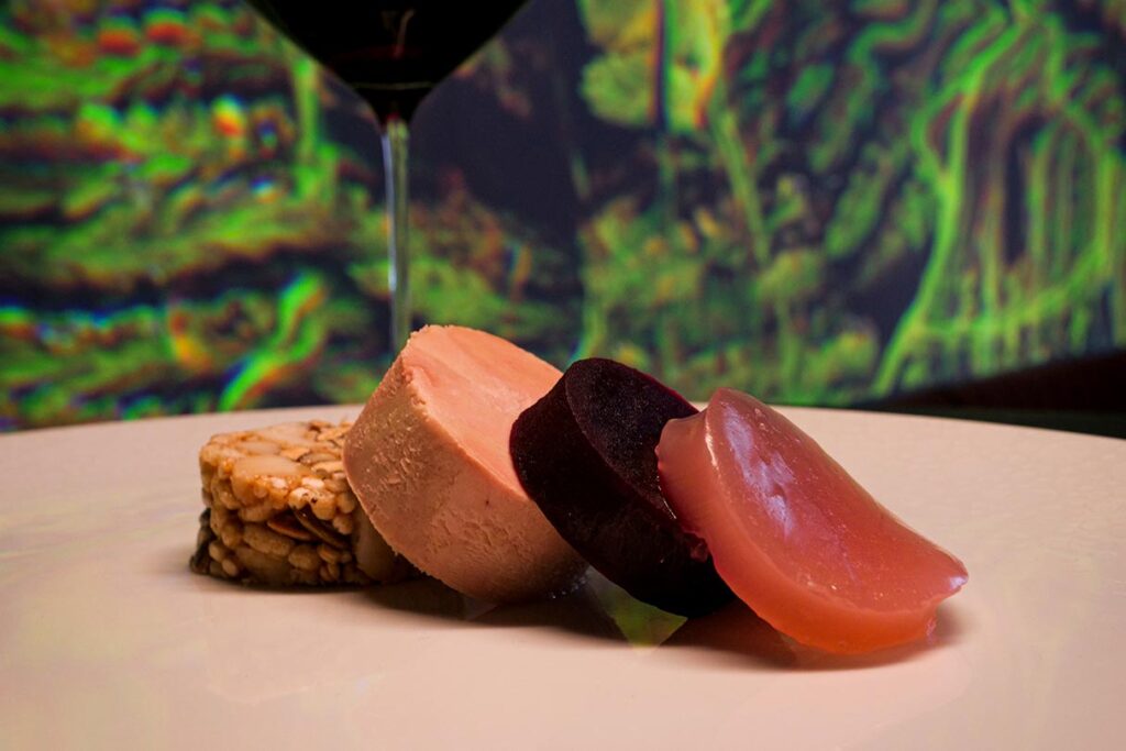Foie gras, beet, macadamia, sakura medallions with a glass of red wine and Katherine Melançon artwork in the blurry background
