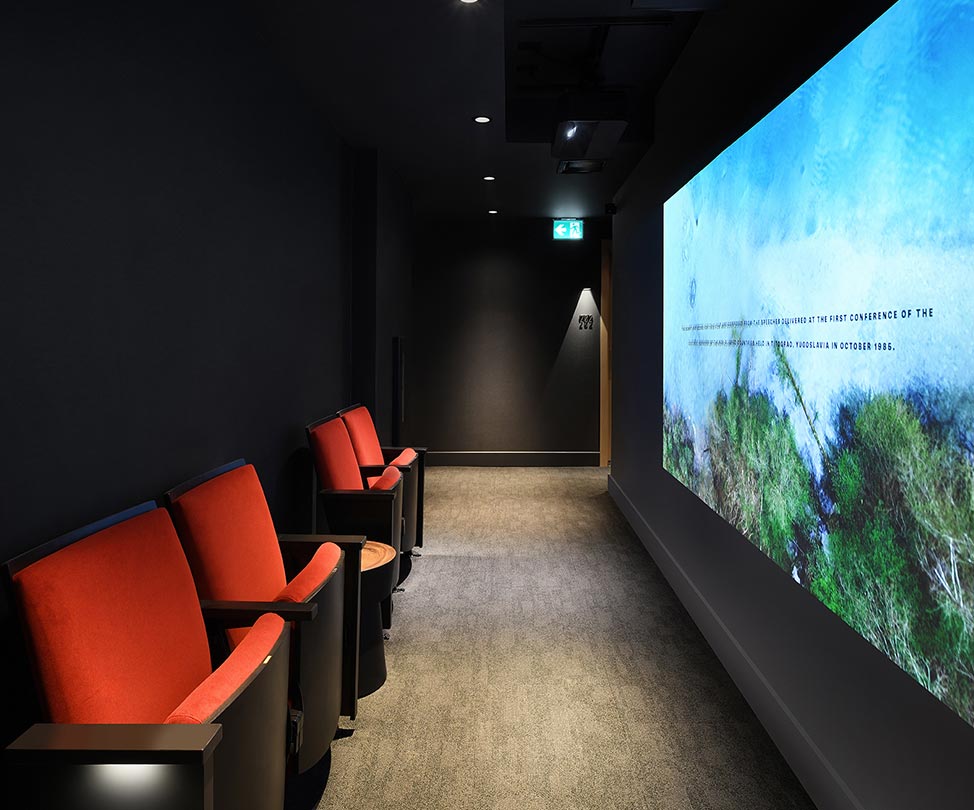 Lux exhibition space with theatre chairs and projection in the hallway to the rooms
